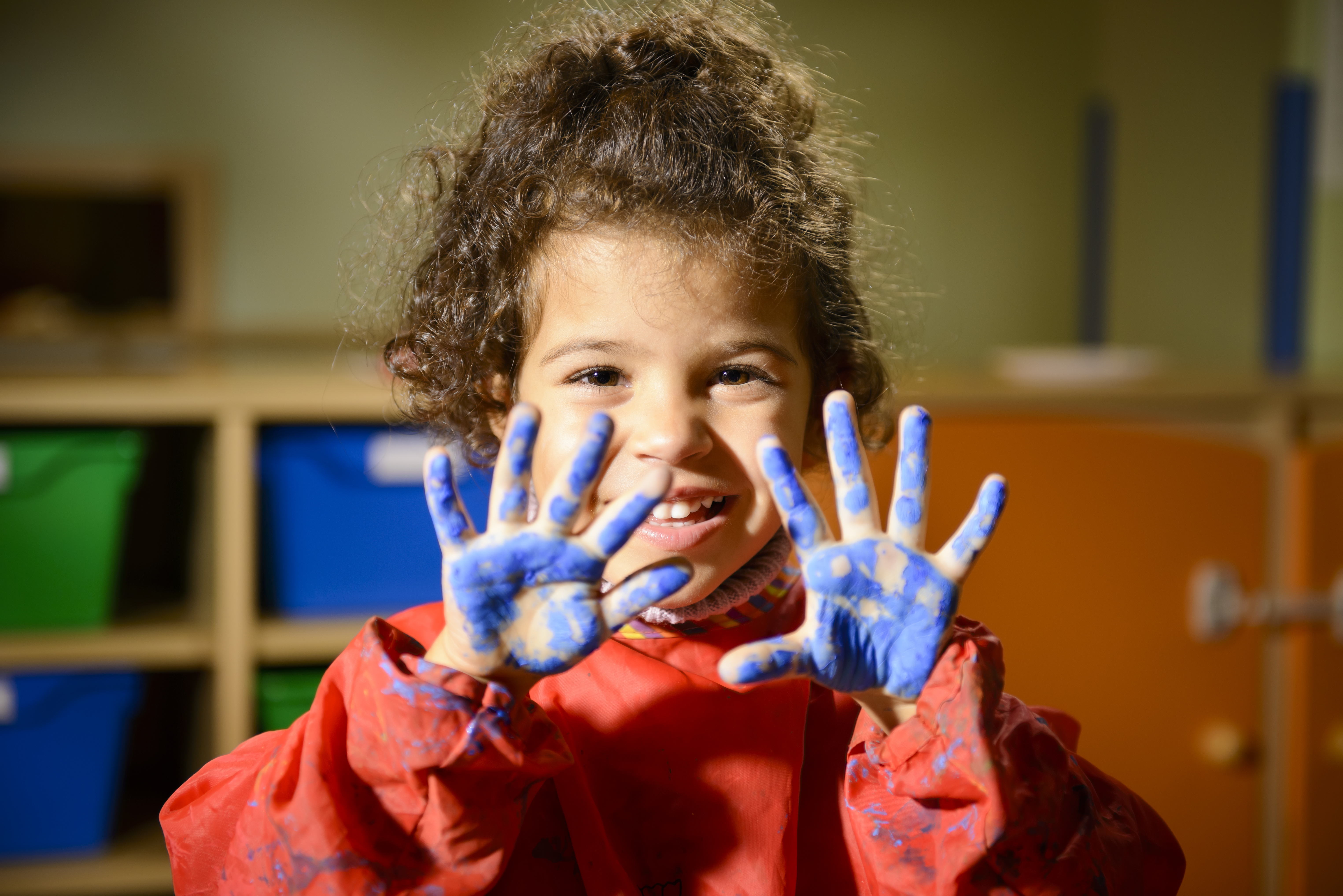 Happy little girl painting with hands in kindergarten