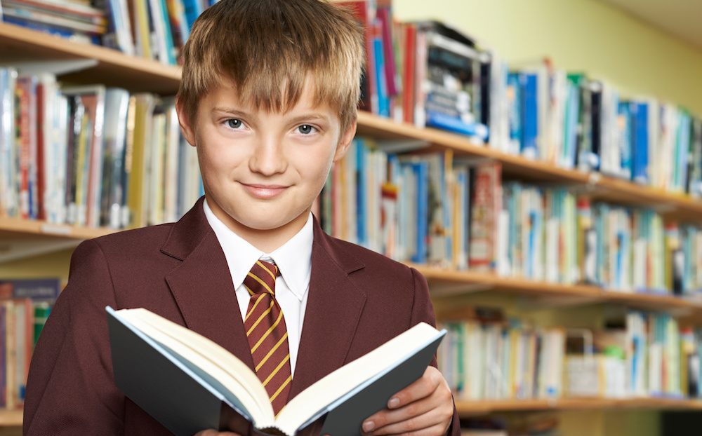 Boy Wearing School Uniform Reading Book In Library