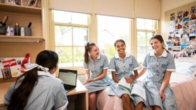 Four teenaged girls in blue and white school uniforms sitting in a school boarding house bedroom, laughing