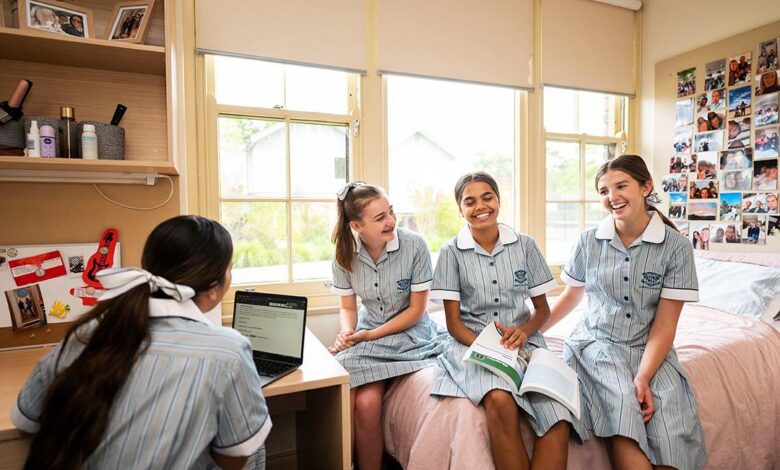 Four teenaged girls in blue and white school uniforms sitting in a school boarding house bedroom, laughing
