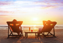 Two people relaxing in deck chairs on the beach at sunset