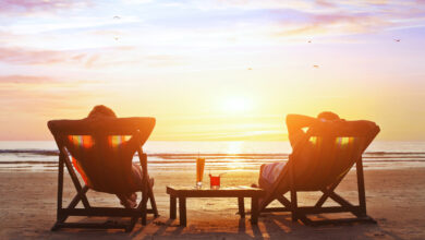 Two people relaxing in deck chairs on the beach at sunset