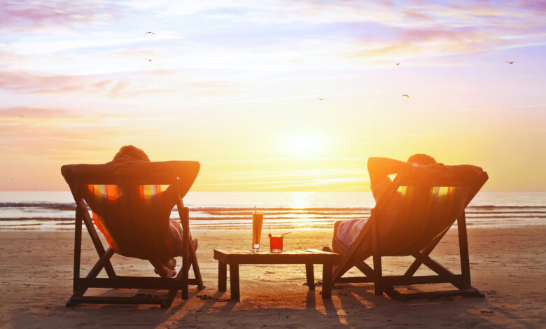 Two people relaxing in deck chairs on the beach at sunset