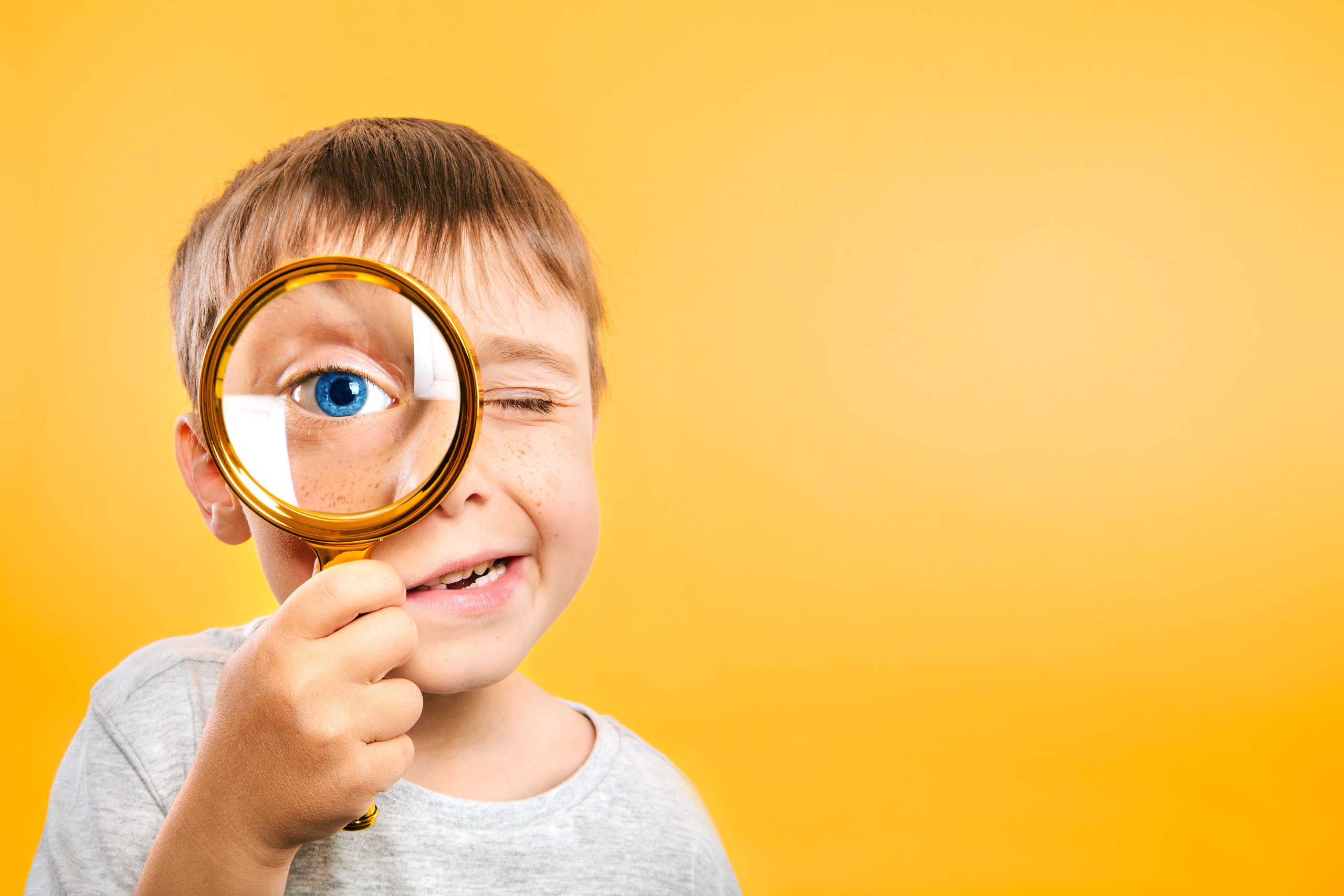 Child with magnifying glass on yellow background