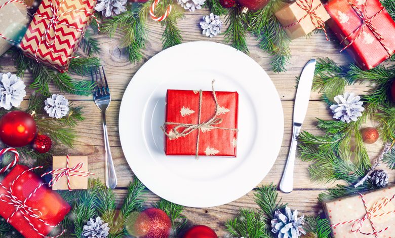 Festive table setting with wrapped gift on dinner plate, with knife and fork on either side